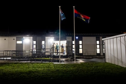 Picture of new Joint Cadet Centre. Two ACF cadets stand on the door looking out into the night whilst flags from the ACF and RAFAC fly high.