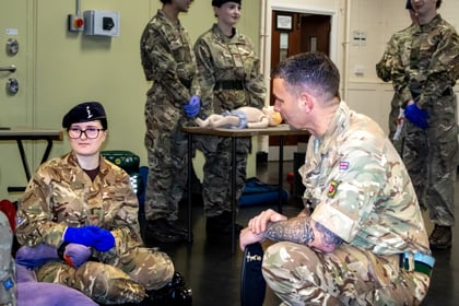 ACF Officer crouching in uniform watching a cadet apply a tourniquet