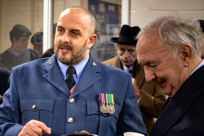 Warrent Officer in formal uniform holding a chocolate cup cake whilst talking with dignitaries.