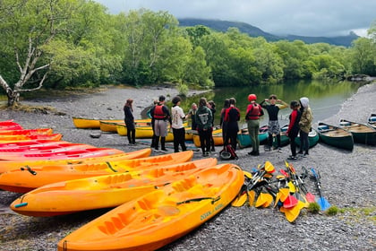 group of cadets stood by a river with 7 yellow, orange and red Kayaks