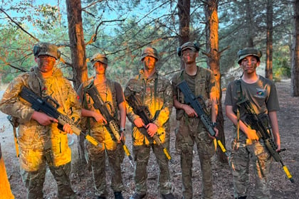 Five people in camouflage uniforms and face paint stand in a wooded area, each holding a rifle with a yellow marker, illuminated by sunlight through the trees during the Berkshire ACF Summer Camp 2026.