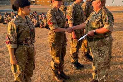 A woman in military uniform shakes hands with a young cadet during a ceremony at the Berkshire ACF Summer Camp 2026, with two other cadets and a group seated in the background on a dry, grassy field.