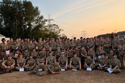 A large group of people in military uniforms pose together outside on grass at sunset, with some sitting and most standing, in front of buildings and trees during the Berkshire ACF Summer Camp 2026.