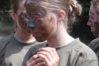 A close up of a cadet applying camouflage paint to their face