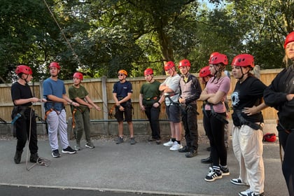 Cadets in helmets are watching an activity. Three cadets on the left hand side are holding onto a rope and looking up towards the side of the camera