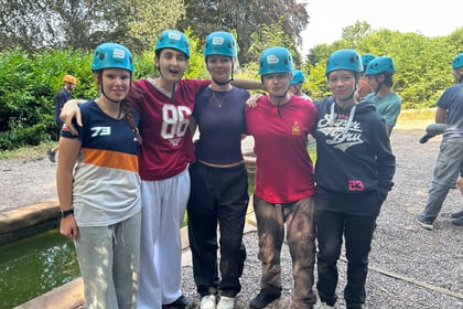 Five cadets, arm in arm, wearing helmets stand and smile for the camera. Other cadets are in the background preparing for an activity.