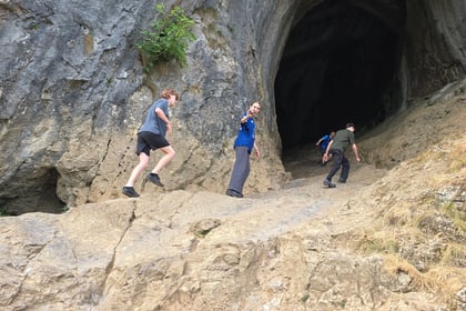 A view of four cadets walking up a large rock formation into the entrance of a cave