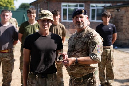 A cadet holds up his promotion badge which is being handed to him by an adult in uniform. Other cadets stand in the background.