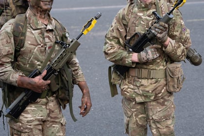 Two cadets in full camouflage smile at the camera. They are stood in a car park in front of some vehicles ready for expedition.