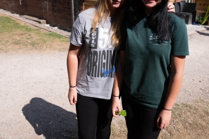 Two cadets in normal clothes pose for the camera outside a brick building with a wooden structure at the front
