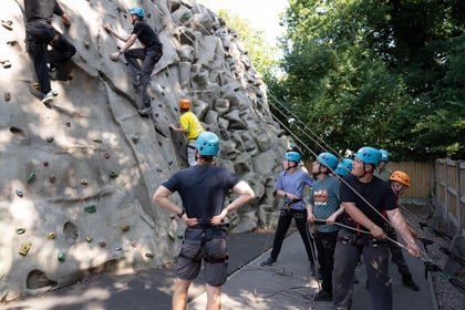 two cadets on a climbing wall with a group of cadets on the ground holding the safety ropes