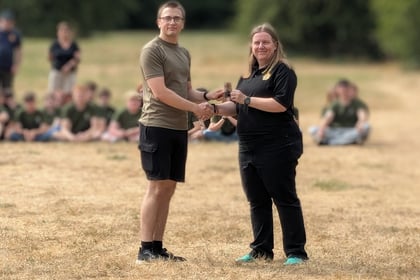 An adult instructor hands a cadet a badge while shaking hands