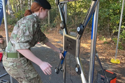A person in military uniform uses a reaction training wall with light-up buttons outdoors under a canopy, surrounded by trees and equipment.