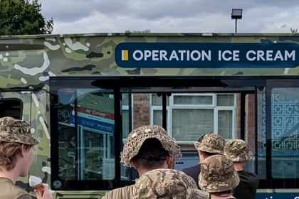 A camouflaged ice cream van labelled Operation Ice Cream is parked, with several people in matching camo hats standing in front, waiting to be served.