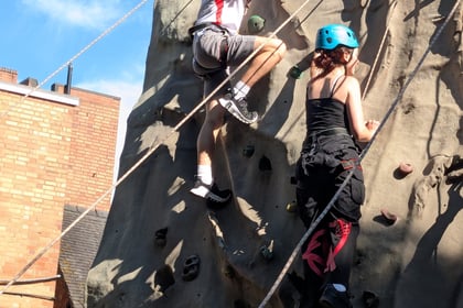 Two young people climb a climbing wall with ropes attached and helmets on