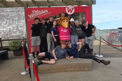 A group of cadets surround a person dressed as a Womble, with two laying across the front of the photo. A sign behind says The Wombles at the Heights of Abraham.