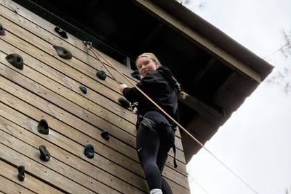A young person at the top of a climbing wall looks down towards the camera