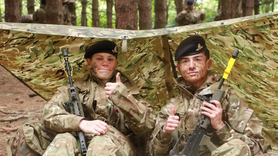 Cadet under a basha with weapons for fieldcraft exercise