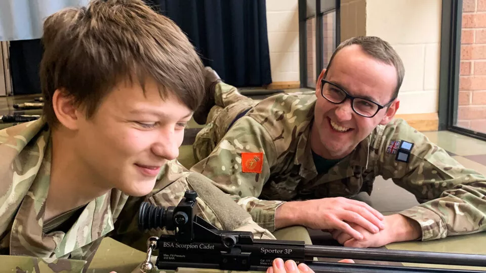 A uniformed instructor shows a cadet how to handle an air rifle.