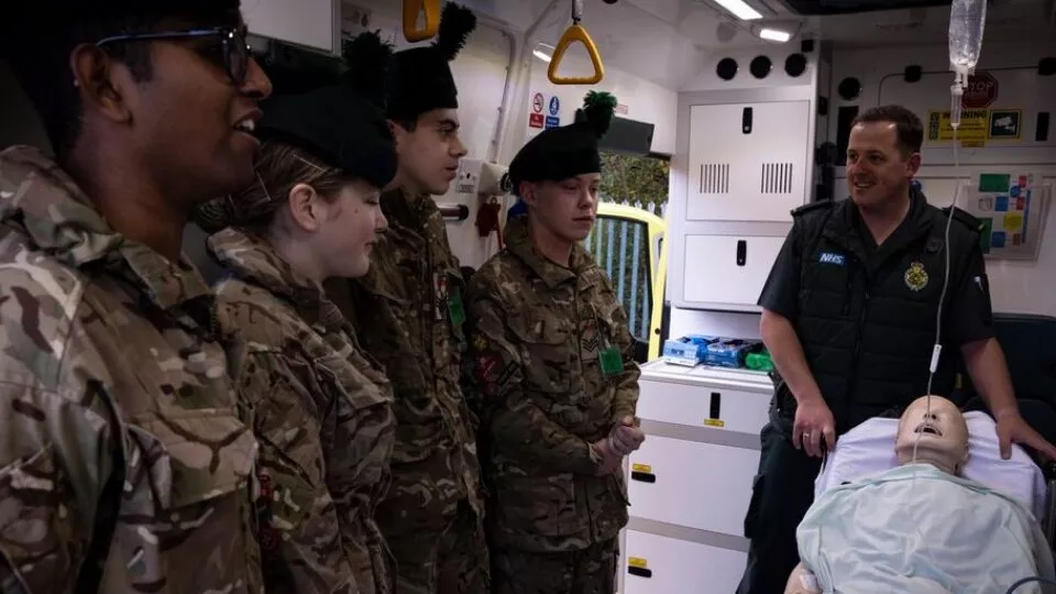 cadets in uniform being shown the inside of an ambulance with fake person on the bed