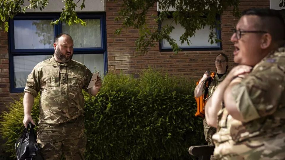 2 adults in military uniform one sat on a bench pretending to choke
