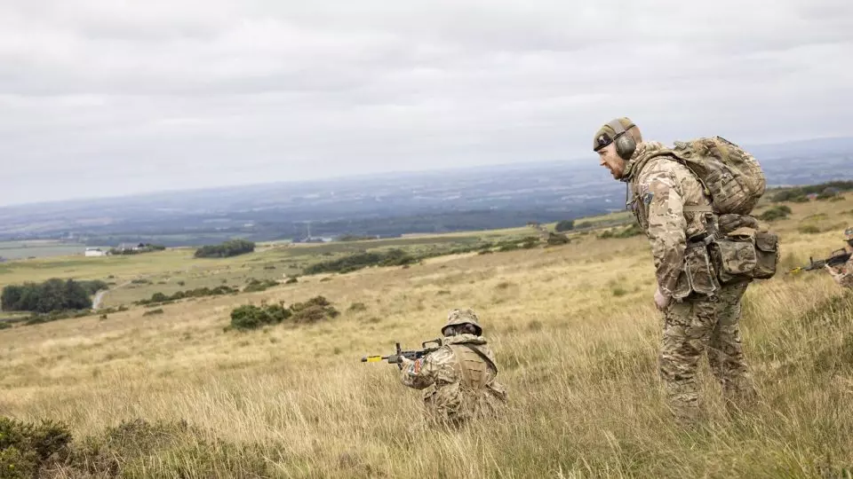 Adult volunteer in uniform wears ear defence during fieldcraft exercise
