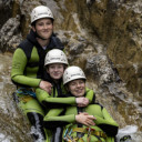 Three cadets wearing white helmets and green and black wetsuits while sliding down a waterfall